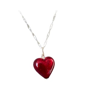 May include: A necklace featuring a silver chain and a red heart-shaped pendant. The heart pendant has a glossy finish. The necklace is shown against a white backdrop.