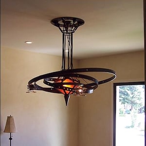 May include: A modern, black metal chandelier with a unique, circular design. The chandelier has multiple light bulbs and a warm, orange-toned light. The chandelier is hanging over a wooden dining table with black chairs.