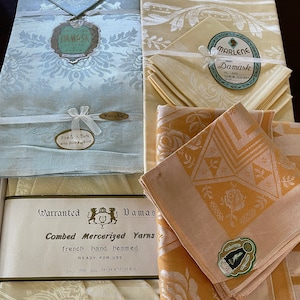 May include: A set of white and light blue damask tablecloths and napkins with a label that reads "Superior Damask" and "Kureha". The set also includes a set of yellow and peach damask tablecloths and napkins with a label that reads "Marlene Impy Damask".