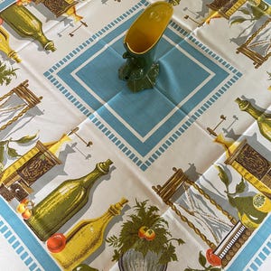 May include: White tablecloth with a blue border and a repeating pattern of bottles, plants, and fruit. A green and yellow ceramic vase sits in the center of the tablecloth.