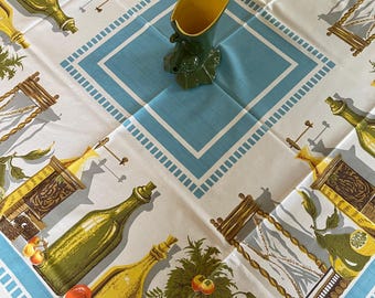 May include: White tablecloth with a blue border and a repeating pattern of bottles, plants, and fruit. A green and yellow ceramic vase sits in the center of the tablecloth.