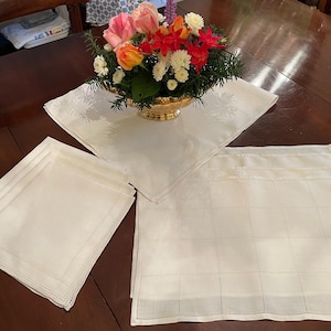 May include: A white tablecloth with a floral design and a set of white linen napkins. The tablecloth has a delicate floral pattern and the napkins are folded neatly.