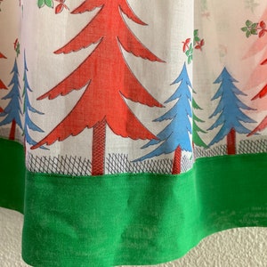 May include: Close-up of a green fabric hem with a white fabric background featuring a repeating pattern of red and blue stylized trees.