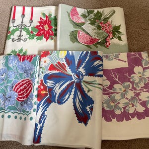 May include: A collection of vintage tablecloths with various patterns. Designs include a Christmas theme with holly and poinsettias, watermelon slices, a large blue bow, floral patterns, and a botanical print with a red pod.