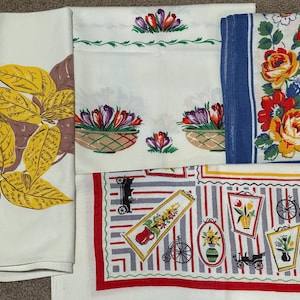 May include: Four vintage tea towels with different floral patterns. One features yellow leaves on a white background, another has a white background with purple and yellow flowers in baskets, a third has a blue background with yellow and red flowers, and the last has a white background with a striped pattern and red, yellow, and gray flowers.