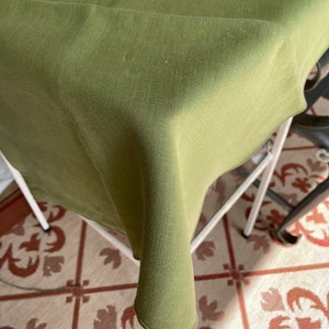 May include: A green tablecloth draped over a table with a white metal frame. The tablecloth is made of a soft, textured fabric and has a subtle sheen.