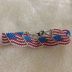 May include: A beaded bracelet with a wavy design featuring the American flag colors of red, white, and blue.