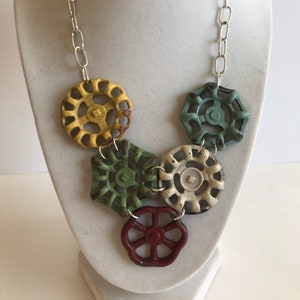 May include: A necklace made from repurposed vintage water valve handles. The necklace features five handles in various colors, including yellow, green, white, and red. The handles are connected by a silver chain.