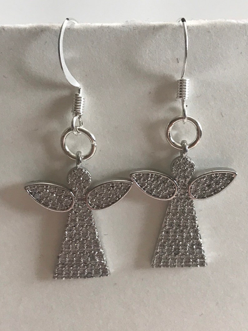 May include: A pair of silver angel earrings with clear crystal accents. The earrings have a hook closure.
