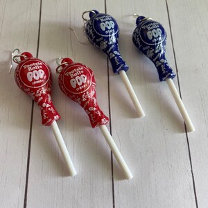 May include: Pair of earrings featuring Tootsie Roll Pop lollipops. One pair is red with cherry flavour and the other is blue with grape flavour.