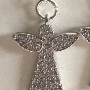 May include: Silver angel earrings with clear crystal accents. The angel is wearing a gown and has wings.