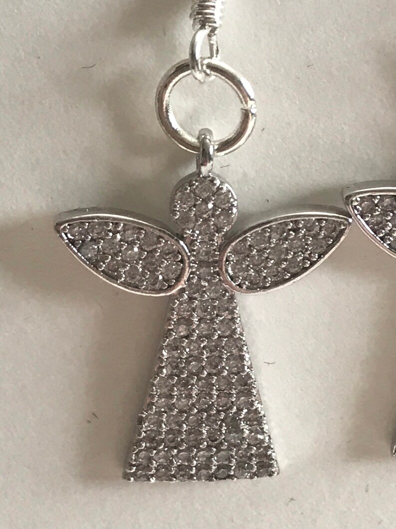 May include: Silver angel earrings with clear crystal accents. The angel is wearing a gown and has wings.