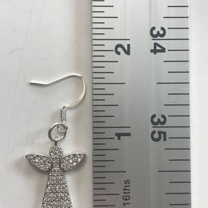 May include: Silver angel earring with clear crystal accents, measured against a ruler. The earring is approximately 1 inch long.