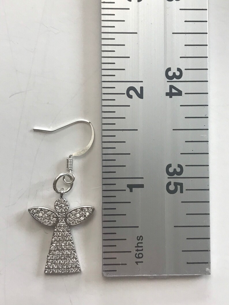 May include: Silver angel earring with clear crystal accents, measured against a ruler. The earring is approximately 1 inch long.