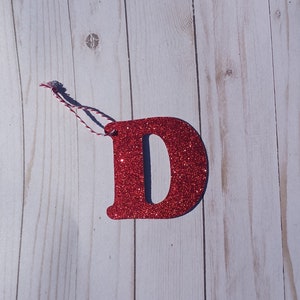 May include: Red glitter letter D ornament with a red and white twine hanger.