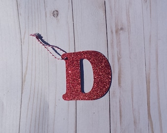 May include: Red glitter letter D ornament with a red and white twine hanger.