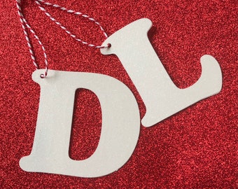 May include: White glitter letters "D" and "L" hanging from a red glitter background with white and red twine.