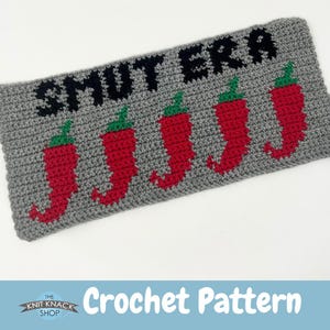 May include: Crochet pattern for a grey and red cushion with the text "Smut Era" and five red chilli peppers.