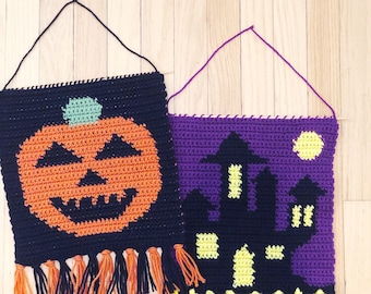 May include: Two crocheted Halloween wall hangings with black yarn and colorful accents. The first features a jack-o'-lantern with orange and green yarn. The second features a black silhouette of a haunted house with yellow windows and a purple background.