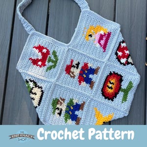 Puede incluir: Bolso tote de ganchillo azul claro con personajes e iconos pixelados de un videojuego popular. El bolso incluye imágenes de Mario, la Princesa Peach y otros elementos del juego. Tiene una correa azul claro a juego y el texto "Crochet Pattern".