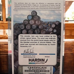 Pu&ograve; includere: Certificato di autenticit&agrave; in una custodia di plastica trasparente. Il certificato presenta un'immagine di botti di legno impilate e testo sull'origine dell'articolo da doghe di botti di whisky Johnnie Walker. Il logo Hardin Penworks &egrave; visibile.
