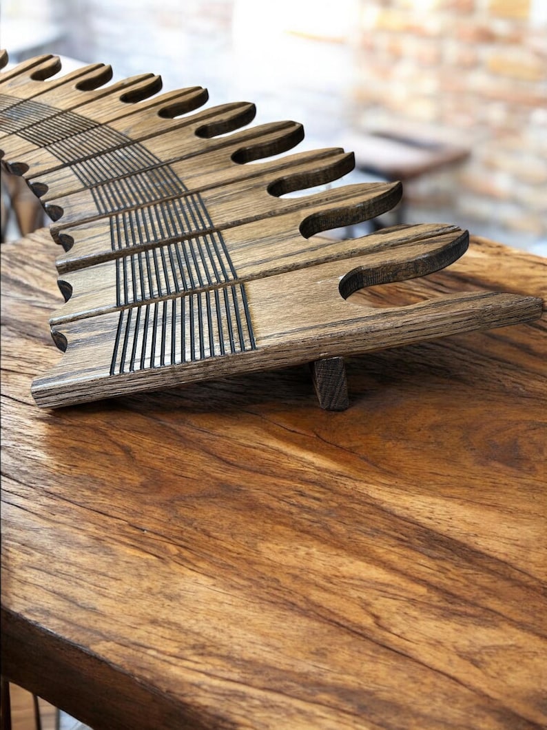 May include: A wooden book stand with a unique design. The stand is made of dark-stained wood and features a series of curved, finger-like supports. The supports are connected by horizontal slats with vertical grooves. The stand is on a wooden surface.