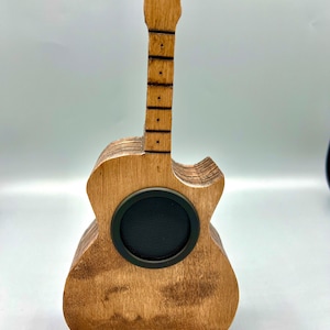 May include: A wooden guitar-shaped speaker with a black speaker grille. The guitar is stained a light brown color.