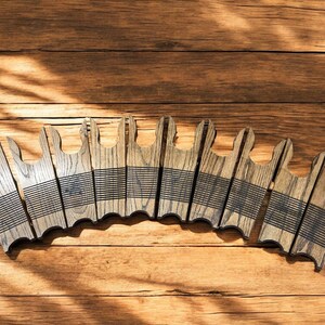 May include: A collection of wooden coasters with a unique design, arranged on a wooden surface. Each coaster is a light brown color with a series of black lines. The coasters have a distinctive shape, adding a touch of rustic charm.