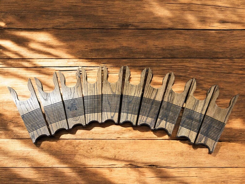 May include: A collection of wooden coasters with a unique design, arranged on a wooden surface. Each coaster is a light brown color with a series of black lines. The coasters have a distinctive shape, adding a touch of rustic charm.