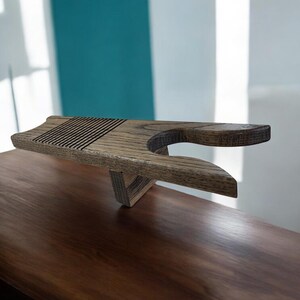 May include: Wooden tea tray with a unique design. The tray is made of light brown wood and features a slatted top surface and a curved handle. The tray is supported by a triangular base, and is designed for serving tea or other beverages.