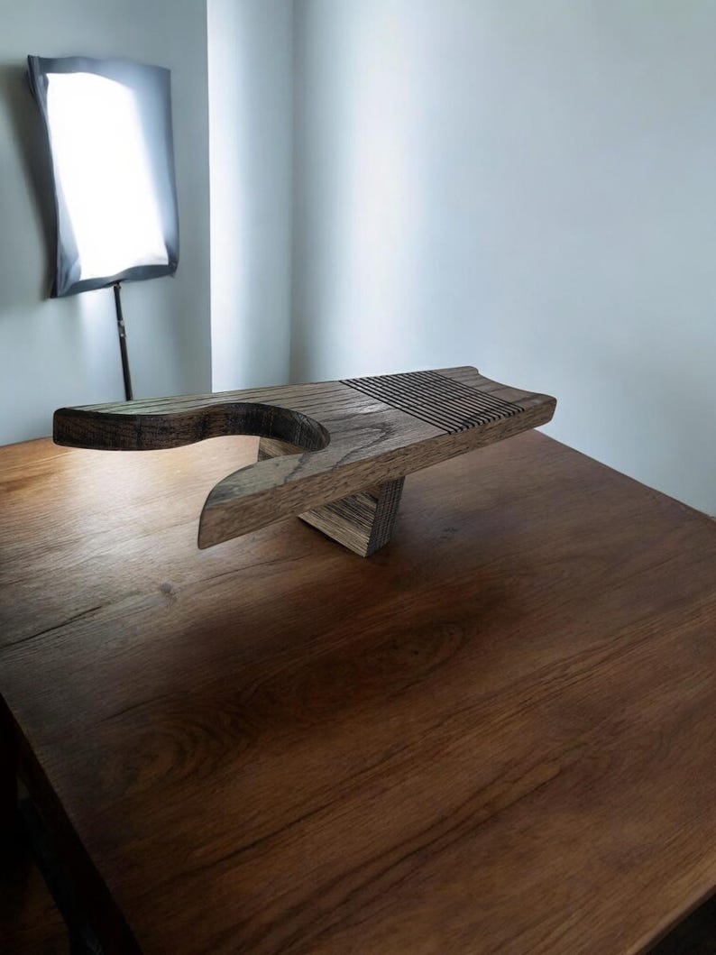 May include: A handcrafted wooden breadboard with a unique design. The board features a curved handle and a grooved section for slicing. The natural wood grain and warm tones create a rustic aesthetic. The breadboard is supported by a triangular base.