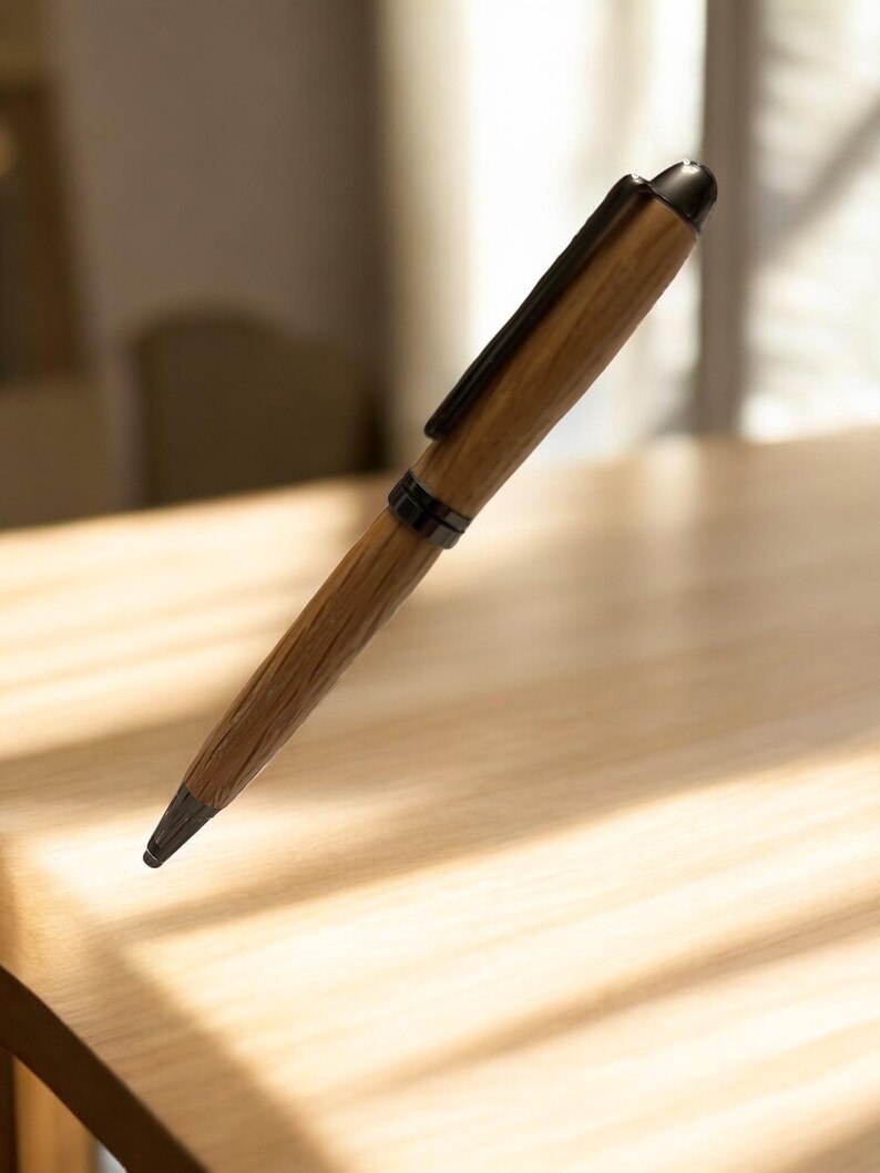Pu&ograve; includere: Una penna in legno con clip e punta in metallo scuro. La penna presenta un motivo a venature naturali e un cappuccio nero. La penna &egrave; appoggiata su una superficie di legno chiaro.