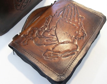 May include: Two brown leather book covers with embossed designs. One cover features a Celtic knot design, while the other has a pair of praying hands with a rosary.