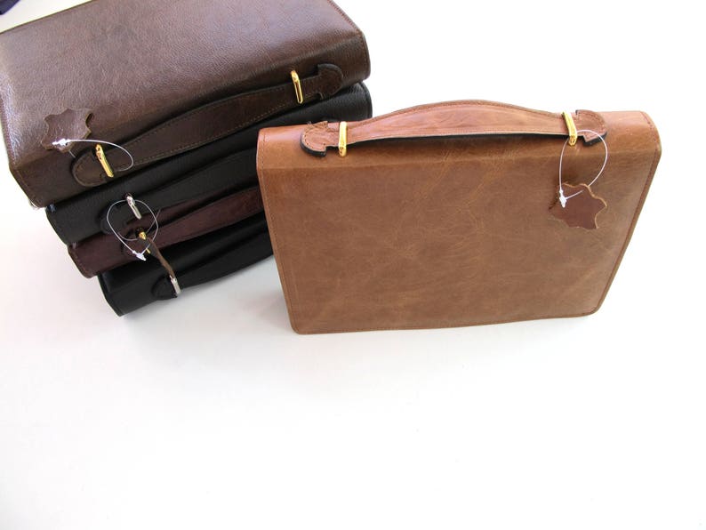 May include: A stack of four leather-bound journals with gold clasps and leather tags. The top journal is brown, the next two are black, and the bottom journal is brown.