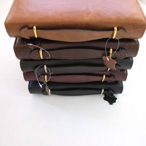 May include: A stack of five leather-bound journals with gold clasps and handles. The journals are in various shades of brown and black.