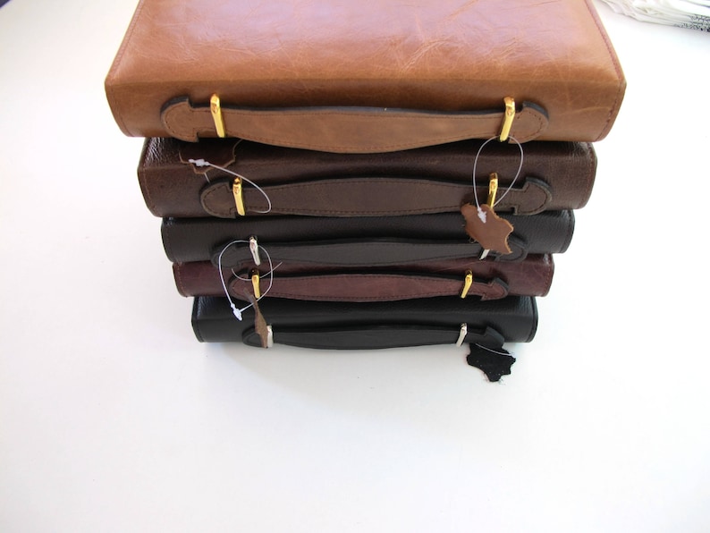 May include: A stack of five leather-bound journals with gold clasps and handles. The journals are in various shades of brown and black.