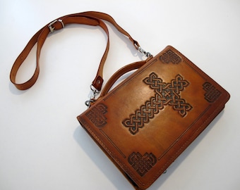 May include: A brown leather bag with a long strap and a Celtic knot cross design. The bag has a flap closure and a handle.