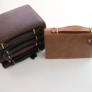 May include: A stack of five brown leather-bound journals with gold clasps and a single brown leather journal with a gold handle.