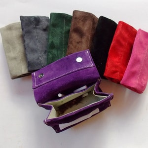 Puede incluir: Un conjunto de diez bolsas de rollo de cigarrillos de gamuza en varios colores, incluyendo morado, gris, verde, marrón, negro, rojo y rosa. Las bolsas están abiertas para revelar el forro interior y una pequeña cantidad de tabaco.