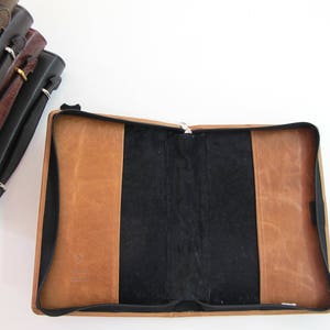May include: A brown leather-bound journal with a black interior and a zipper closure. The journal is open and the pages are blank.