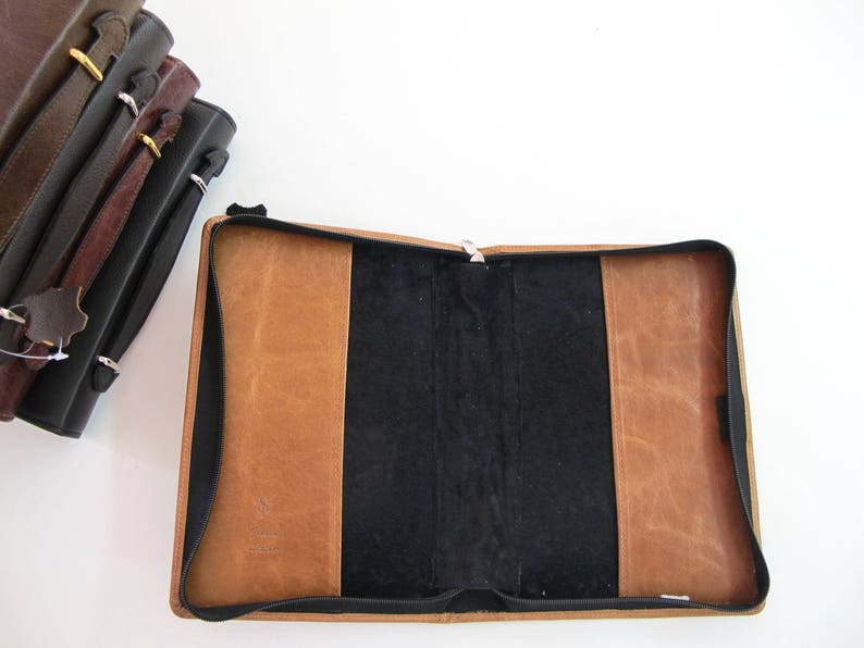May include: A brown leather-bound journal with a black interior and a zipper closure. The journal is open and the pages are blank.