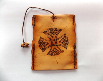 May include: A tan leather pouch with a Celtic cross design. The edges are stitched, and a decorative cross is in the centre. A brown cord and wooden bead are attached for closure. The pouch is likely for storing small items.
