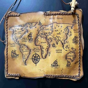 May include: A vintage-style leather map of the world with a compass rose and ships. The map is brown and has a stitched border. The map includes the names of continents and oceans, including North America, South America, Europe, Asia, Africa, Australia, the Arctic Ocean, the Pacific Ocean, the Atlantic Ocean, and the Indian Ocean.