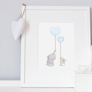 May include: A framed print featuring a watercolor illustration of a gray elephant and a beige bunny holding blue heart-shaped balloons. The artwork is in a white frame, with a white heart-shaped decoration hanging from the top.