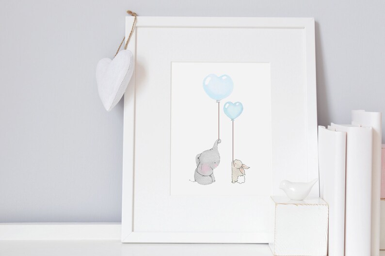 May include: A framed print featuring a watercolor illustration of a gray elephant and a beige bunny holding blue heart-shaped balloons. The artwork is in a white frame, with a white heart-shaped decoration hanging from the top.