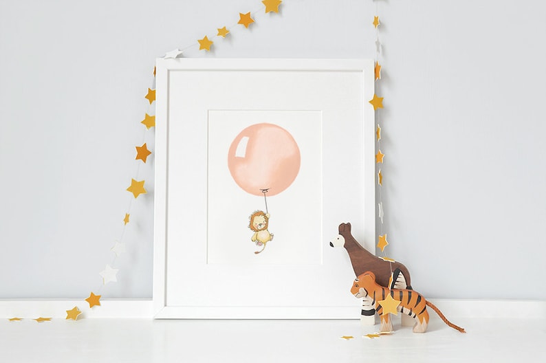 Peut inclure: Une impression encadr&eacute;e d'un lion tenant un ballon rose. L'impression est entour&eacute;e d'un cadre blanc et d'une guirlande d'&eacute;toiles dor&eacute;es.