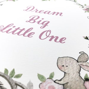 May include: A white card with a pink floral border and the text "Dream Big Little One" in pink script. The card features a watercolor illustration of a rabbit and a hedgehog.