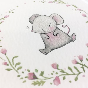 May include: A watercolor illustration of a cute gray mouse with pink accents, walking inside a wreath of green leaves and pink flowers.