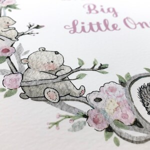 May include: A watercolor illustration of a wreath with a bear, a rabbit, and a hedgehog. The wreath is made of branches and flowers. The text "Big little one" is written in pink lettering.