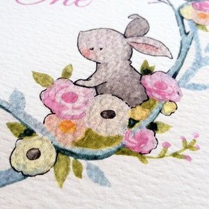 May include: A watercolor illustration of a gray bunny sitting on a branch with pink, yellow, and white flowers. The bunny is surrounded by green leaves and the branch is painted in a light blue color.
